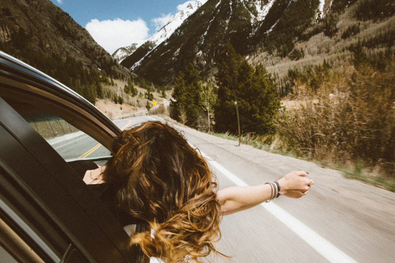 rapariga a viajar de carro pelo meio da natureza com a cabeça fora da janela