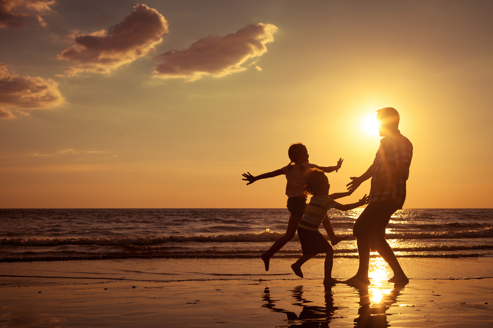 praia com pai e filhos a brincar ao por do sol